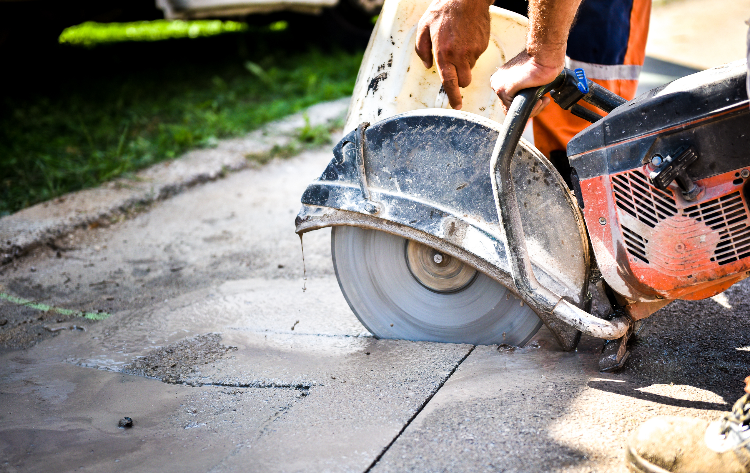 Construction worker cutting Asphalt paving stabs for sidewalk using a cut-off saw. Profile on the blade of an asphalt or concrete cutter with workers shoes and protective gear.