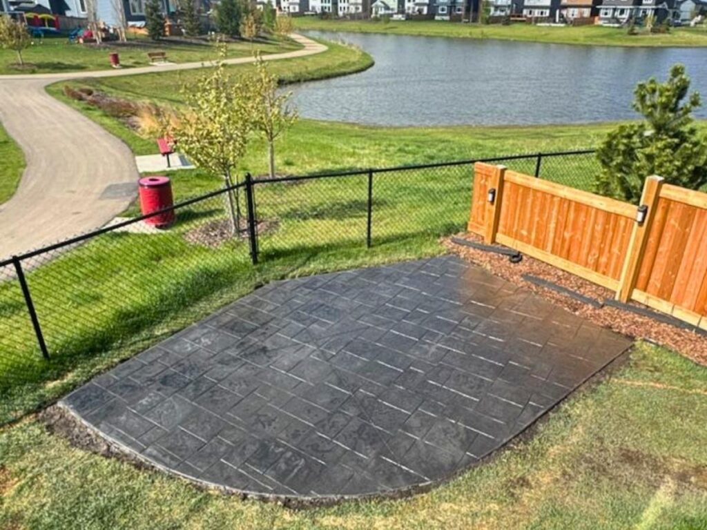A premium stamped concrete backyard patio poured by Stele Concrete featuring a hot tub and scenic view.